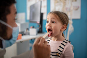 male doctor checking little girl's throat in his office