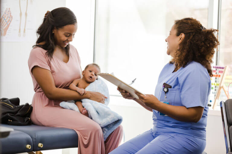 New mother looks down at son as pediatrician smiles