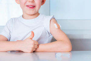 Vaccination and immunization of population concept. Kid boy with plaster on arm after vaccinated. Smiling child after inoculated. New Normal