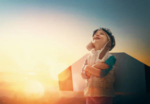 Little child playing pilot. Girl on the background of sunset sky. Kid in an astronaut costume dreaming of becoming a spaceman.