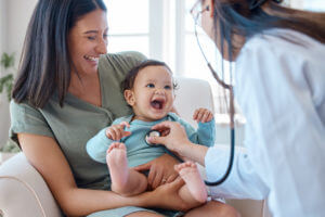 baby sitting on her mother's lap while being examined by a Pediatrician