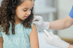 nurse is giving the girl a chilld vaccine using a needle