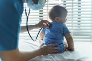 female Pediatrician doctor examining her little baby patient with stethoscope in medical room