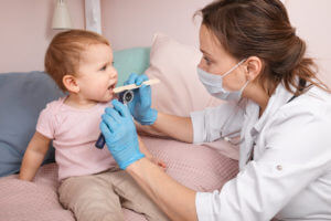 A pediatrician is examining a baby girl at home for a sore throat infection.