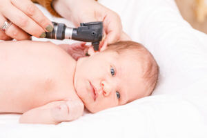 During a newborn ENT exam, a doctor checks the ears of an infant with an otoscope for signs of ear infection in a pediatric clinic.
